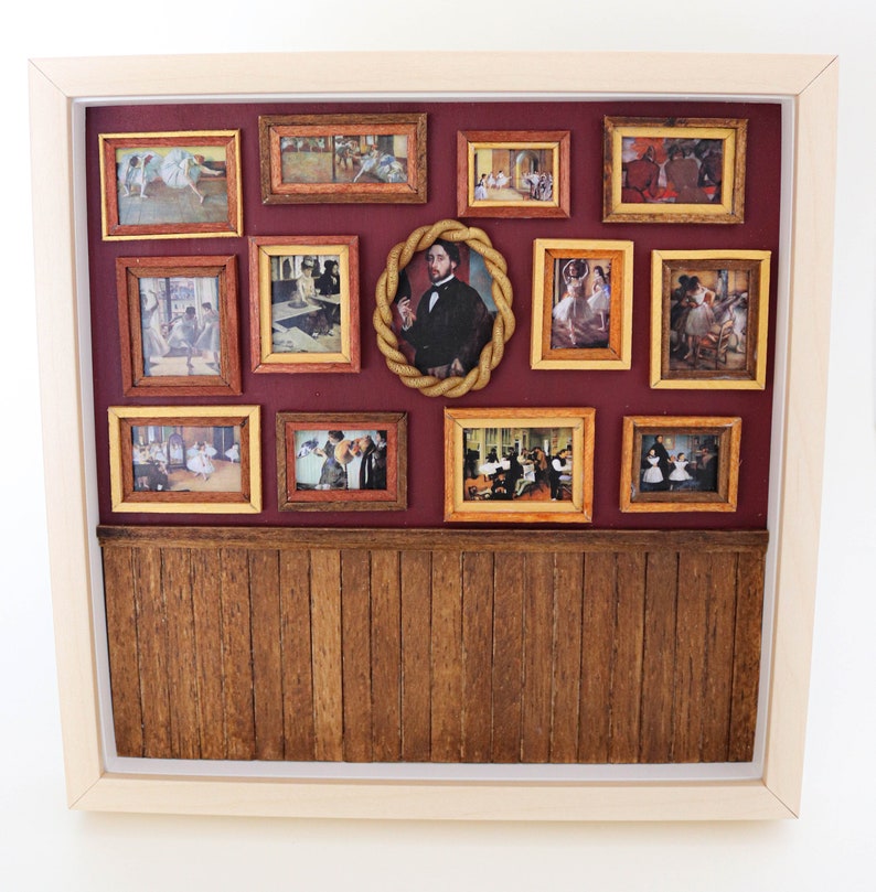May include: A miniature dollhouse room with a burgundy wall and a wood-paneled floor. The wall is decorated with 12 framed pictures of dancers and a portrait of a man.