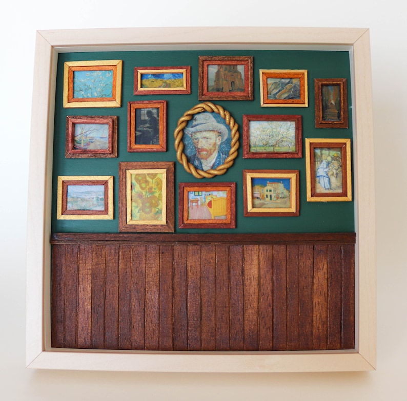 May include: A framed artwork with a green background and a collection of smaller framed paintings inside. The smaller paintings are of various subjects, including landscapes, portraits, and still lifes. The larger frame is made of wood and has a light brown finish.