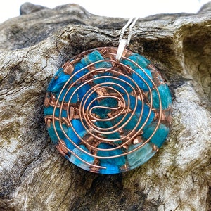 Pode incluir: Um colar com um pingente redondo com um design de espiral de fio de cobre e cristais azuis e verdes incrustados em resina transparente.