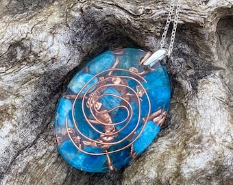 May include: A blue and copper pendant with a spiral design. The pendant is made of resin and features a copper wire spiral embedded in the resin. The pendant is on a silver chain.
