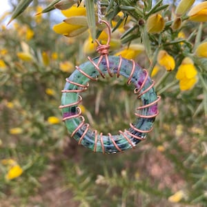 May include: A green and pink gemstone pendant wrapped in copper wire. The pendant is shaped like a circle and is hanging from a chain.