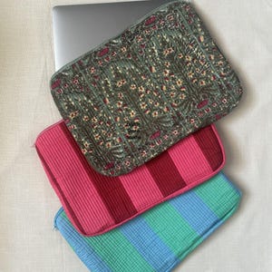 Puede incluir: Tres fundas para portátil en diferentes patrones. La funda superior es verde con estampado floral. La funda del medio es rosa con rayas rojas. La funda inferior es azul con rayas verdes. Las fundas están hechas de tela acolchada.
