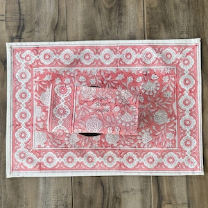 Può includere: Un sottopiatto rettangolare con stampa floreale rosa e bianca. Il sottopiatto presenta un bordo con motivi floreali ripetuti e il testo "Jaipur Store Studio". Il centro del sottopiatto presenta un motivo floreale.