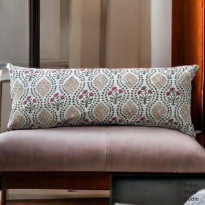 May include: A long, rectangular throw pillow with a white background and a repeating pattern of brown and pink floral motifs. The pillow is sitting on a light purple couch.