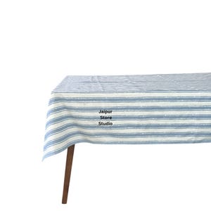 May include: A blue and white striped tablecloth with a subtle distressed look. The tablecloth is draped over a wooden table.