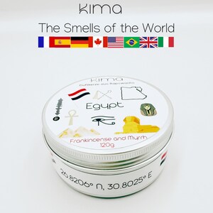 Peut inclure: Une boîte à bougie ronde argentée avec le texte "Kima" et "The Smells of the World". Le couvercle présente le mot "Egypt" avec des illustrations et le texte "Frankincense and Myrrh, 120g". Des coordonnées sont imprimées en bas.