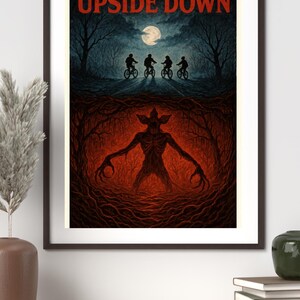 Könnte beinhalten: Gerahmter Kunstdruck mit dem Text "THE UPSIDE DOWN". Er zeigt Radfahrer auf einer Straße unter einem mondbeschienenen Himmel und eine Kreatur in einer feurigen, wurzelgefüllten Umgebung. Das Kunstwerk ist in einem schwarzen Rahmen gerahmt.