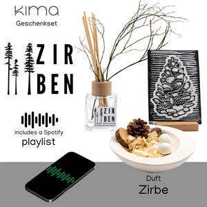 Può includere: Un set regalo con un diffusore in vetro trasparente con bastoncini di legno, una stampa di pigna in bianco e nero e una ciotola bianca con elementi decorativi. Il set include una playlist Spotify. Il testo "Zirben" è visibile.