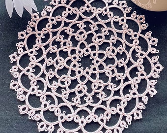 May include: A delicate pink crocheted doily with a circular design. The doily is made of fine thread and has a intricate pattern of loops and knots.