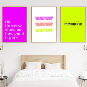 May include: Three framed prints with motivational quotes. The left print is pink with white text that reads "OK Universe, show me how good it gets". The middle print is white with pink text that reads "I am the luckiest person I know". The right print is neon green with black text that reads "For the good of us, and with a smile to home, EVERYTHING I DESIRE is already on its way to me."