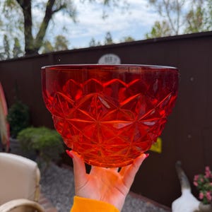 May include: A vibrant red glass bowl featuring a geometric diamond-cut pattern across its exterior surface. The bowl has a wide, circular opening and a tapered base, with a translucent finish that allows light to pass through the faceted glass structure.