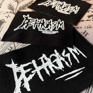 Peut inclure: Trois écussons de tissu noir avec texte brodé blanc. Le texte est stylisé et semble être un logo de groupe ou un design similaire. Les écussons sont rectangulaires et ont une texture tissée.