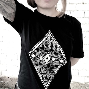 May include: A black short-sleeved t-shirt featuring a large, white, diamond-shaped graphic print on the chest. The graphic consists of intricate, repeating geometric patterns, including horizontal lines, small squares, and triangles.