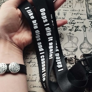 Pode incluir: Dois cordões pretos com texto branco. O texto em um cordão diz "Oops I dig it again!" e o texto no outro cordão diz "I like big digs and I cannot lie..."