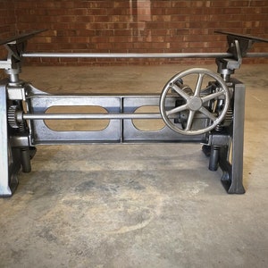 May include: A gray metal table base with a crank and adjustable height. The base is made of cast iron and has a vintage industrial look.