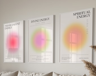 May include: Three framed art prints with the words "Transcedent Energy", "Divine Energy", and "Spiritual Energy" in black text. Each print features a colorful, blurred aura design in shades of red, pink, yellow, and orange. The prints are displayed above a beige sofa.