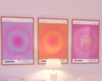 May include: Three framed posters with a gradient background of pink, orange, and purple. Each poster has a circle in the center and text below the circle. The text on the posters reads "Support", "Soul", and "Balance". The posters are hanging on a white wall above a white dresser with a lamp and a white chair.