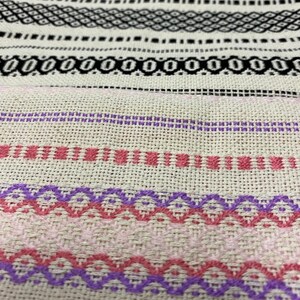 May include: Close-up of a woven fabric with a pattern of pink and purple stripes. The fabric has a natural, off-white colour.