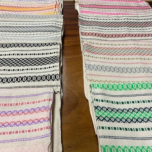 May include: A stack of colourful woven placemats with geometric patterns in shades of pink, green, black, white and grey.