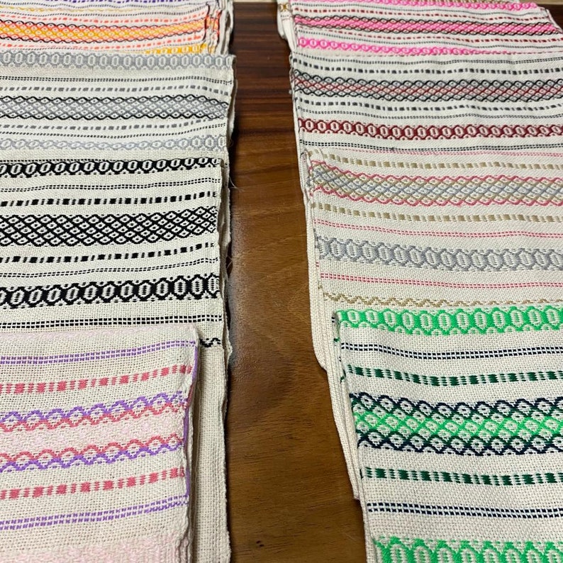 May include: A stack of colourful woven placemats with geometric patterns in shades of pink, green, black, white and grey.