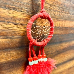 May include: Red dreamcatcher with a copper wire web and red feathers. The dreamcatcher has a red suede cord and white beads.
