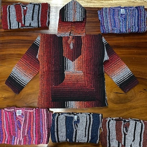 May include: A selection of Baja hoodies in various colours and striped patterns. The hoodies have a pullover design with a hood and a front pocket. Colours include red, orange, black, blue, purple, and grey. The hoodies are made of woven fabric.