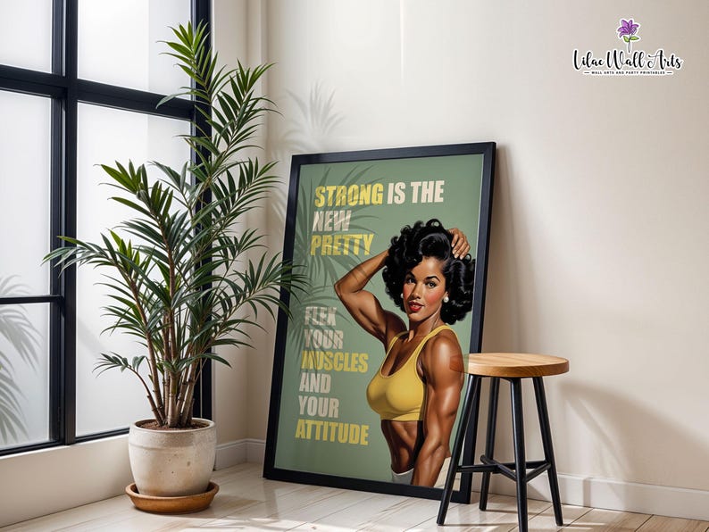 May include: A framed wall art print featuring a muscular person with dark hair wearing a yellow sports bra. The text reads: STRONG IS THE NEW PRETTY, FLEX YOUR MUSCLES AND YOUR ATTITUDE. The background is sage green with palm leaf silhouettes.