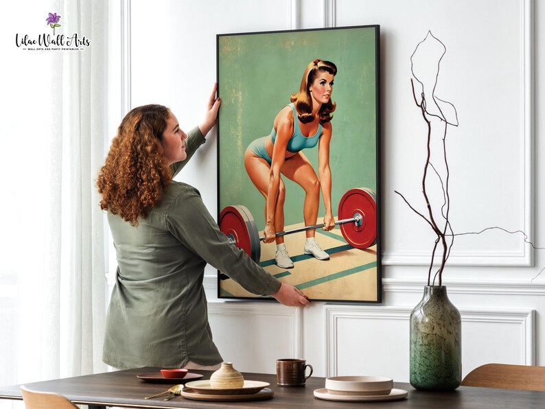 May include: A vintage style poster featuring a woman lifting a barbell. The woman is wearing a blue and white swimsuit and has blonde hair. The background is a light green color. The poster is framed in black.