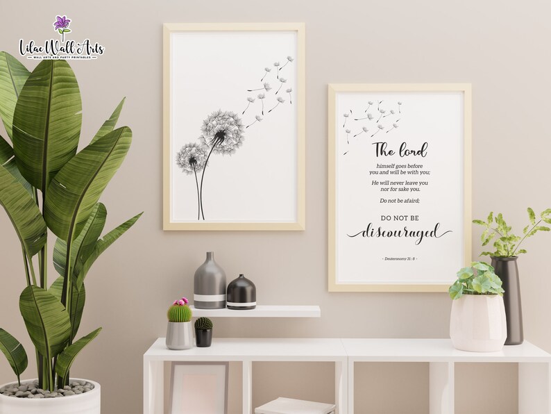 May include: Two framed prints with a white background. The print on the left features a black and white illustration of a dandelion with seeds blowing in the wind. The print on the right features a black and white text quote from Deuteronomy 31:8, "The Lord himself goes before you and will be with you. He will never leave you nor forsake you. Do not be afraid. Do not be discouraged."