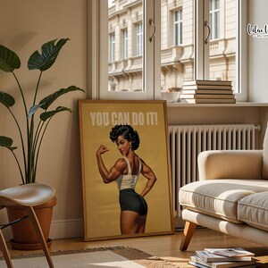 May include: A rectangular wall art print featuring a retro-style illustration of a person flexing their arm muscles. The person wears a white tank top and black shorts. The text YOU CAN DO IT! is printed in white at the top of the tan-colored poster.