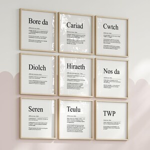 May include: Nine framed prints with black text on white backgrounds, each featuring a different word and definition. The frames are light-colored wood, and the prints are arranged in a 3x3 grid on a light pink wall.
