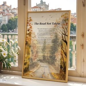 May include: A framed print of Robert Frost's poem "The Road Not Taken" with a watercolor illustration of a path through a forest. The print has a gold frame and is displayed on a windowsill with a view of a city. A pot of daisies is in the foreground.