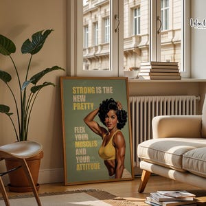 May include: A rectangular wall art print in a wooden frame featuring a vintage-style illustration of a muscular person with dark curly hair wearing a yellow sports bra. The text reads: STRONG IS THE NEW PRETTY, FLEX YOUR MUSCLES AND YOUR ATTITUDE.