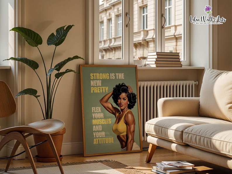 May include: A rectangular wall art print in a wooden frame featuring a vintage-style illustration of a muscular person with dark curly hair wearing a yellow sports bra. The text reads: STRONG IS THE NEW PRETTY, FLEX YOUR MUSCLES AND YOUR ATTITUDE.
