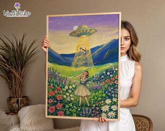 May include: A framed art print featuring a retro-style illustration of a person in a polka dot dress standing in a vibrant flower field, looking up at a flying saucer beaming down a cat. The scene includes purple mountains and a starry sky.