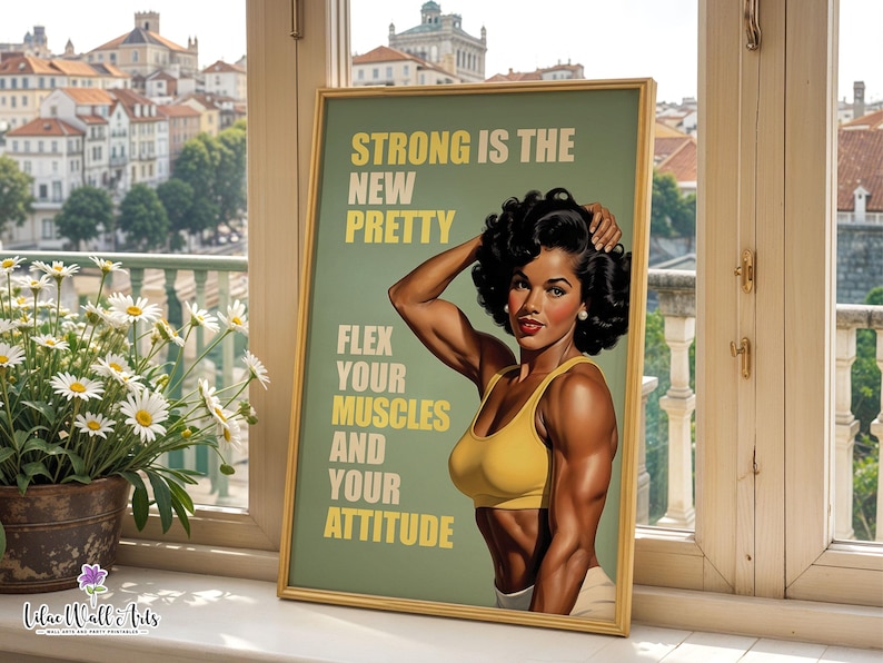 May include: A framed poster featuring a muscular person with dark curly hair wearing a yellow sports bra. The text reads: STRONG IS THE NEW PRETTY. FLEX YOUR MUSCLES AND YOUR ATTITUDE. The background is sage green with yellow lettering.