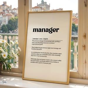 May include: A framed wall art print featuring a dictionary-style definition of the word manager in black text on a cream background. The text describes a manager as someone who oversees tasks, guides a team, and bridges strategy and execution.