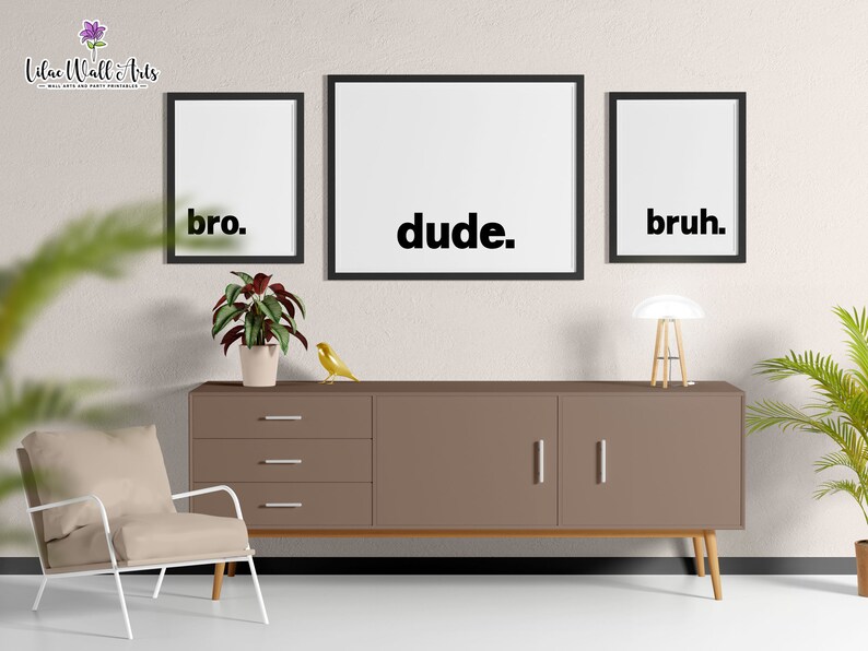 May include: Three black framed prints with white backgrounds and black text. The prints read "bro." "dude." and "bruh." The prints are hanging on a beige wall above a brown dresser with three drawers and two doors. A white chair with wooden legs is in the foreground.