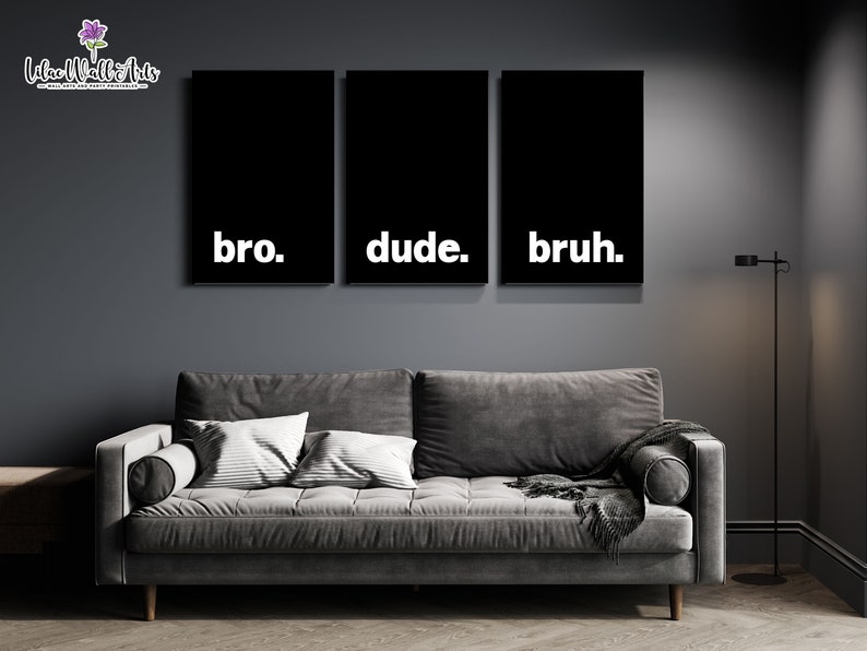 May include: Three black framed canvas prints with white text. The text on the prints reads "bro", "dude", and "bruh". The prints are hanging on a dark gray wall above a gray couch.