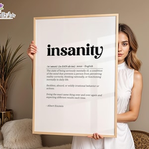 May include: A rectangular wall art print in a light wood frame featuring the word insanity in bold black text, followed by its phonetic pronunciation, definition, and a quote attributed to Albert Einstein on a white background.