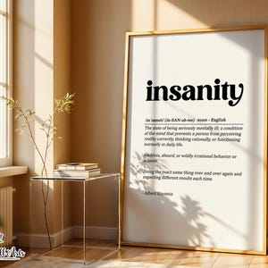 May include: A framed vertical wall art print featuring a dictionary-style definition of the word insanity in black serif and sans-serif typography on a cream background, including phonetic pronunciation and a quote attributed to Albert Einstein.