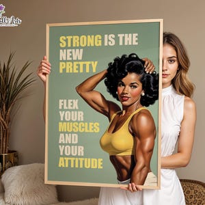 May include: A rectangular framed wall art print featuring a vintage-style illustration of a muscular person with dark curly hair wearing a yellow sports bra. The text reads: STRONG IS THE NEW PRETTY, FLEX YOUR MUSCLES AND YOUR ATTITUDE in yellow.
