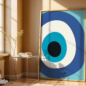 May include: A framed print with a bold eye design. The artwork features concentric circles in blue, white, and black against a light blue backdrop. The gold-coloured frame complements the artwork, displayed in a room with natural light.