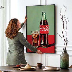 May include: A framed print of a Coca-Cola bottle and a glass of cola with ice. The background is a green and red color scheme.