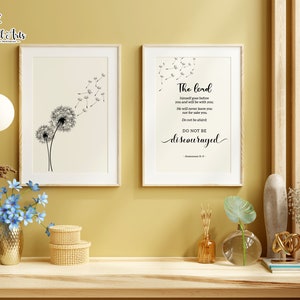 May include: Two framed prints on a wall. The print on the left features a black and white illustration of a dandelion with seeds blowing in the wind. The print on the right features a black and white text quote: "The Lord himself goes before you and will be with you. He will never leave you nor forsake you. Do not be afraid. Do not be discouraged." Deuteronomy 31:8
