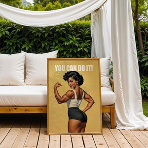 May include: A rectangular poster in a wooden frame featuring a muscular person with dark hair styled in curls, wearing a white tank top and black shorts, flexing their arm. The text YOU CAN DO IT! is printed in white at the top on a tan background.