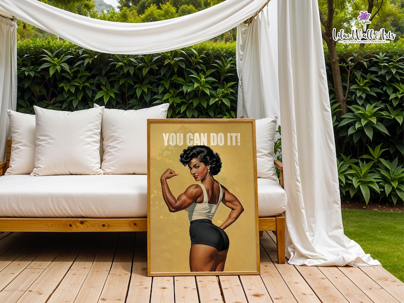 May include: A rectangular poster in a wooden frame featuring a muscular person with dark hair styled in curls, wearing a white tank top and black shorts, flexing their arm. The text YOU CAN DO IT! is printed in white at the top on a tan background.