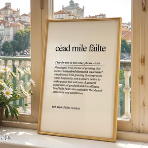 Può includere: Una stampa artistica da parete incorniciata con la frase irlandese céad mile fáilte in testo nero su sfondo crema. La definizione spiega che la frase significa centomila benvenuti, esprimendo ospitalità. La cornice è sottile e dorata.