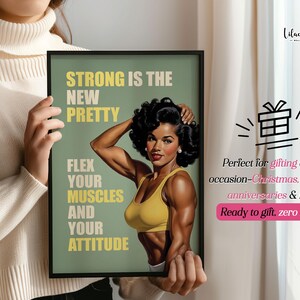 May include: A framed wall art print featuring a muscular person with dark curly hair wearing a yellow sports bra. The text reads: STRONG IS THE NEW PRETTY, FLEX YOUR MUSCLES AND YOUR ATTITUDE. The background is a muted olive green with a black frame.