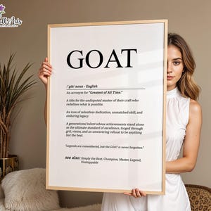May include: A rectangular wall art print in a light wood frame featuring the word GOAT in large black letters at the top. Below the word, the text defines GOAT as an acronym for Greatest of All Time, followed by a descriptive paragraph and the phrase Legends are remembered, but the GOAT is never forgotten, ending with see also: Simply the Best, Champion, Master, Legend, Unstoppable.